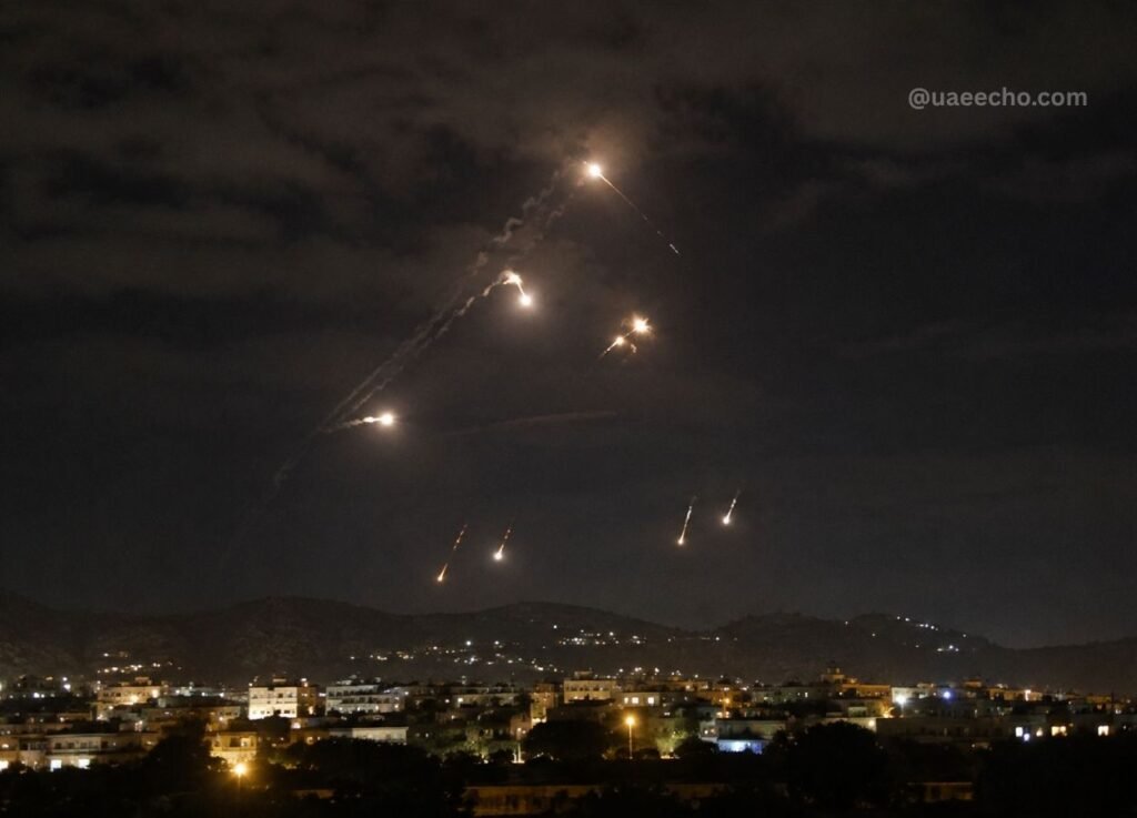 - UAE Echo Nighttime scene of colorful fireworks streaking across a cloudy sky above a lit town and distant hills.