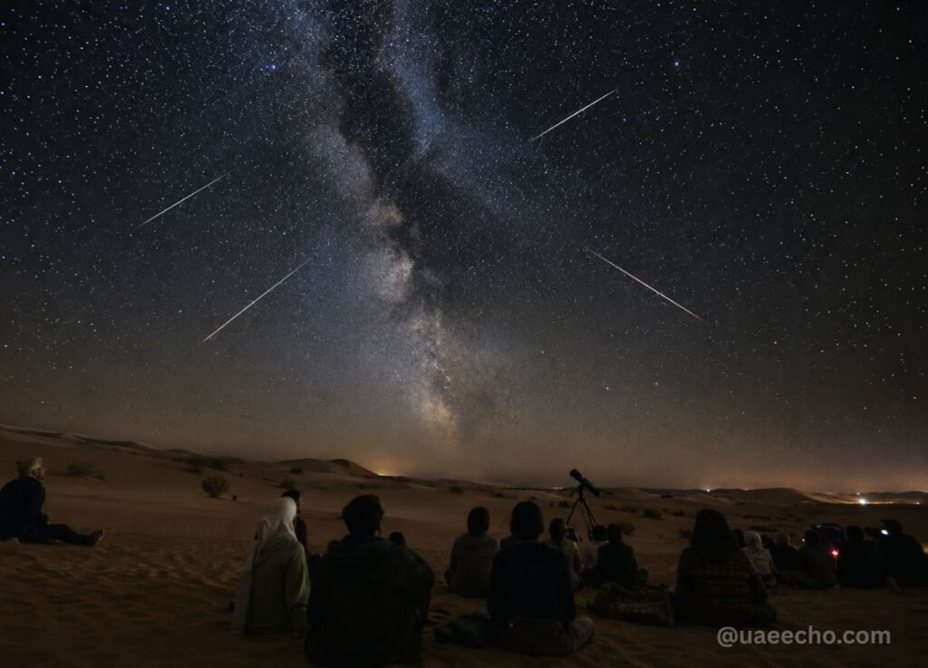 Group of people sitting on desert sand under a star-filled night sky, with the Milky Way visible and meteor streaks? (astronomy night)
