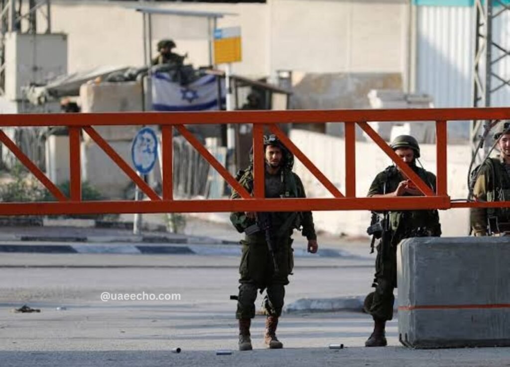 uaeechocom 58 - UAE Echo Armed soldiers stand behind an orange barrier at a checkpoint, with a flag in the background and a concrete barrier nearby.